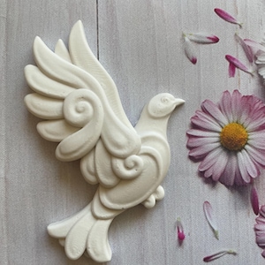 May include: White ceramic dove with intricate detailing on its wings, against a light wood background with pink flower petals scattered around it.