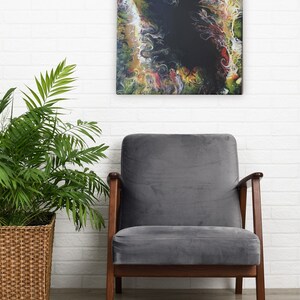 Pode incluir: Pintura abstrata com cores que giram em verde, amarelo, vermelho e branco em torno de um centro preto. A pintura est&aacute; pendurada em uma parede de tijolo branco acima de uma poltrona cinza com pernas de madeira.