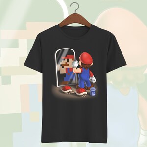 May include: A black t-shirt with a graphic of a video game character looking in a mirror. The character is holding a paintbrush and a can of paint. The mirror shows a pixelated version of the character.