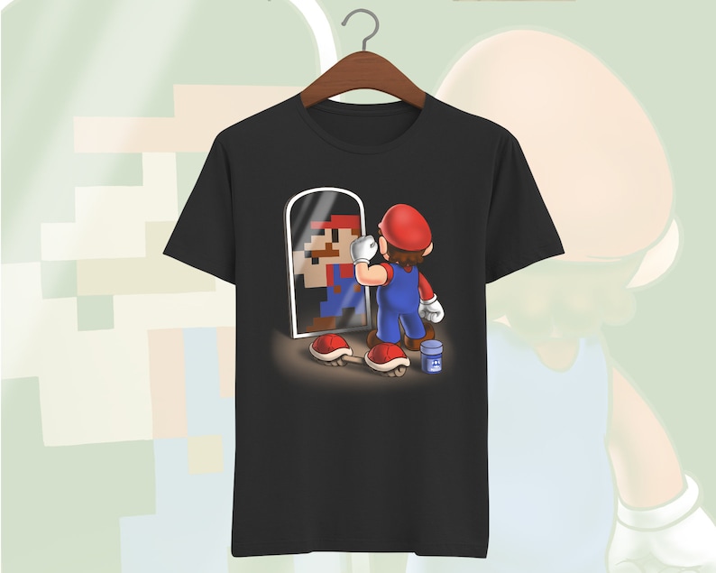 May include: A black t-shirt with a graphic of a video game character looking in a mirror. The character is holding a paintbrush and a can of paint. The mirror shows a pixelated version of the character.