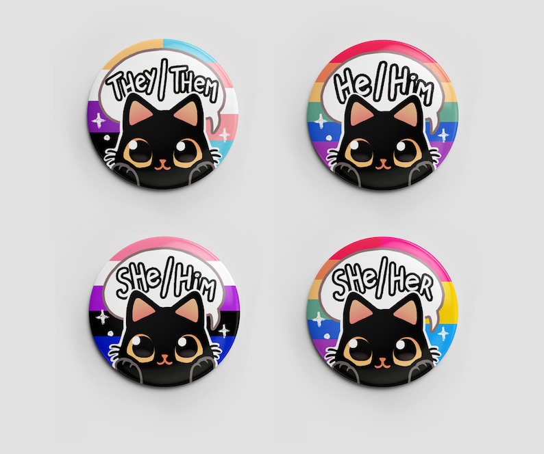 Puede incluir: Cuatro botones redondos con ilustraciones de gatos negros y banderas arco&iacute;ris del orgullo. Los botones muestran el texto "They/Them", "He/Him", "She/Him" y "She/Her".