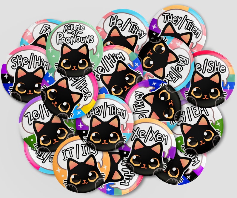 Puede incluir: Una colecci&oacute;n de 14 botones redondos con gatos negros y varias combinaciones de pronombres, incluyendo "She/Him", "He/They", "They/Them", "Xe/Xem", "It/Its", "Ask Me My Pronouns" y "Fae/Fae". Cada bot&oacute;n tiene un fondo colorido con un dise&ntilde;o de arco&iacute;ris.