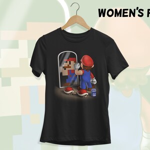 May include: Black t-shirt with a graphic of a pixelated Mario character looking in a mirror at a cartoon Mario character holding a paintbrush. The text "WOMEN'S FIT" is in the upper right corner of the image.