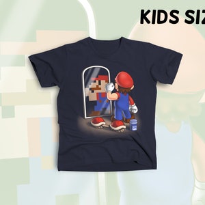 May include: A navy blue t-shirt with a graphic of a pixelated Super Mario character looking in a mirror at a realistic Super Mario character. The text "KIDS SIZE" is in white letters at the top of the image.