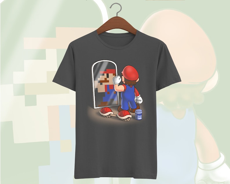 May include: A dark gray t-shirt with a graphic of a video game character looking in a mirror. The character is holding a paintbrush and is surrounded by red and white mushrooms.