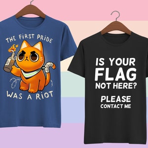 Puede incluir: Dos camisetas con dise&ntilde;os diferentes. La primera camiseta es azul con un gato de dibujos animados sosteniendo un c&oacute;ctel Molotov encendido y el texto "La primera marcha del orgullo fue un mot&iacute;n". La segunda camiseta es negra con el texto "&iquest;Tu bandera no est&aacute; aqu&iacute;? Por favor, contacta conmigo".