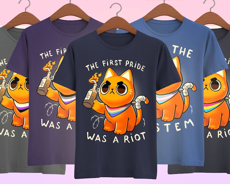 Puede incluir: Cinco camisetas con un gr&aacute;fico de un gato de dibujos animados sosteniendo un c&oacute;ctel Molotov. El texto en las camisetas dice "The First Pride Was A Riot" y "The System Was A Riot".