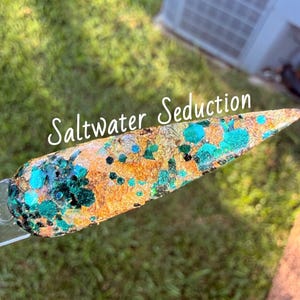 May include: A pointed nail art display tip featuring a textured surface with gold foil flakes, teal and dark green hexagonal glitter, and black specks. The text Saltwater Seduction is printed in white across the center of the nail tip.