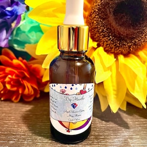 May include: A small glass bottle with a gold cap and a white dropper. The bottle is labelled "Dip Hustle" with a blue diamond and the text "April Showers Bring May Flowers Candle Oil".