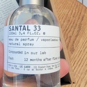 May include: Clear glass SANTAL 33 eau de parfum bottle with a silver cap. The label reads "100ml 3.4 FL.OZ. e" and "natural spray." The text also states "Compounded: in our lab" and "Fresh: 12 months after first."