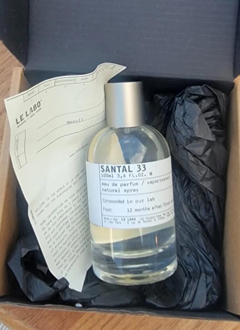 May include: A clear glass bottle of Santal 33 eau de parfum, 3.4 fl oz, with a silver cap, inside a cardboard box. The label includes the text "natural spray." The box contains black tissue paper and a receipt.