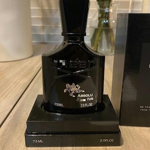 May include: A black perfume bottle with a geometric design, presented on a black box. The bottle has a dark cap and the text "CREED" is visible. The bottle is labeled "ABSOLU RUS" and contains 75 ml (2.5 fl oz).
