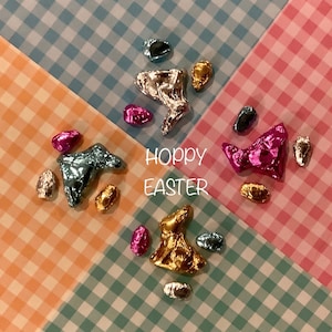 May include: A colorful Easter-themed image with the text "Hoppy Easter" in the center. The image features foil-wrapped chocolate bunnies in various colors, including gold, silver, pink, and blue, arranged in a symmetrical pattern on a checkered background.