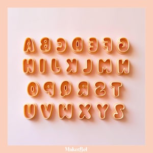 May include: A set of twenty-six light orange plastic alphabet cookie cutters arranged in four rows. Each letter from A to Z is represented in a rounded, sans-serif font style with a thick border, designed for cutting shapes out of dough.