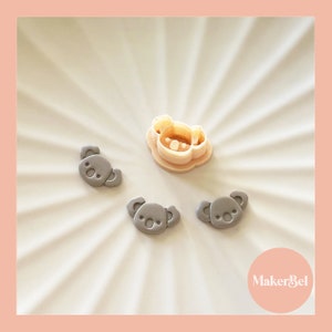 May include: Three gray koala cookie cutters and one larger koala cookie cutter in a light beige color. The cookie cutters are on a white surface with a sunburst pattern. The text "MakerBel" is in the lower right corner of the image.