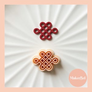 May include: Two red and orange plastic cookie cutters shaped like a traditional Chinese knot, on a white plate with the text "MakerBel" in the bottom right corner.
