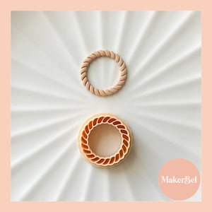 May include: Two beige plastic cookie cutters in the shape of a rope circle. The smaller cutter is on top of the larger cutter.
