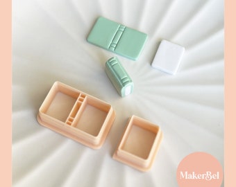 May include: A set of four plastic molds for making miniature books. The molds are in two different colors: light pink and light green. The molds are arranged on a white surface. MakerBel is printed on the surface.
