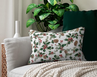 May include: A white throw pillow with a green holly and red berry pattern. The pillow is on a white couch with a green throw blanket.