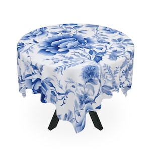 May include: A white tablecloth with a blue floral pattern. The tablecloth is round and has a scalloped edge. It is draped over a table with black legs.