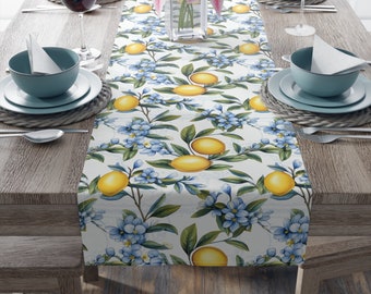 May include: A white table runner with a lemon and blue flower pattern. The runner is on a wooden table with two place settings on each side.