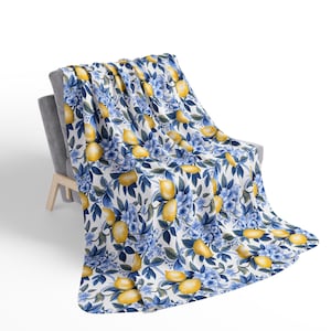 Könnte beinhalten: Eine weiße Decke mit einem Zitronen- und blauen Blumenmuster. Die Decke liegt über einem Stuhl.