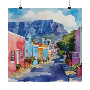 Peut inclure: Une peinture à l'aquarelle représentant des maisons colorées bordant une rue dans une ville avec une montagne en arrière-plan. Les maisons sont peintes dans des tons de rose, bleu, jaune et vert. La montagne est d'un bleu foncé et se trouve au loin. La rue est pavée et bordée de quelques arbres.