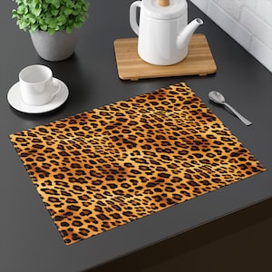 May include: A brown and orange leopard print placemat with a black background. The placemat is made of fabric and has a slightly textured surface.