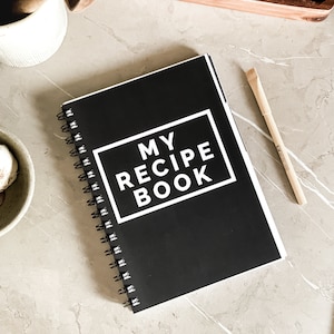 May include: A black spiral bound notebook with the text "MY RECIPE BOOK" in a white rectangle on the front cover.