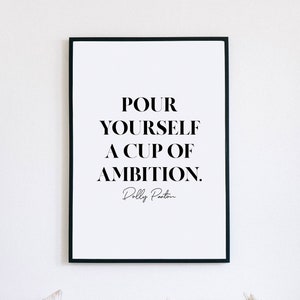 May include: A black and white framed print with the quote "Pour yourself a cup of ambition." by Dolly Parton.