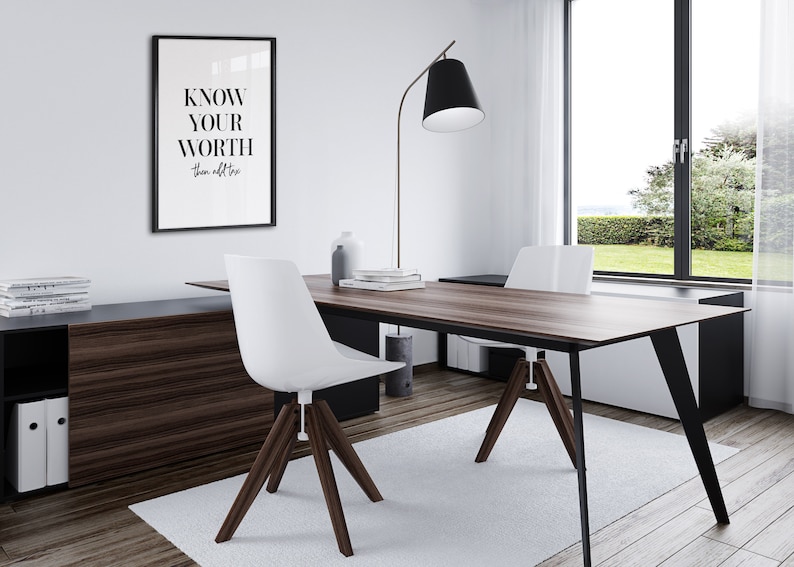 May include: A modern home office featuring a wooden desk and two white chairs. A framed print with the text "KNOW YOUR WORTH" is displayed on the wall. A black floor lamp with a white shade stands in the corner.