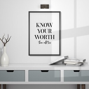 May include: Black and white framed print with the text "KNOW YOUR WORTH then add tax". The print is hanging on a white wall above a white dresser with two drawers.