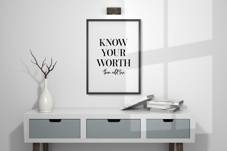 May include: Black and white framed print with the text "KNOW YOUR WORTH then add tax". The print is hanging on a white wall above a white dresser with two drawers.