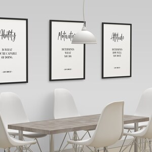 May include: Three black framed motivational posters with white text on a white wall. The posters are titled "Ability", "Motivation", and "Attitude". The text on the posters reads: "Ability is what you're capable of doing", "Motivation determines what you do", and "Attitude determines how well you do it".