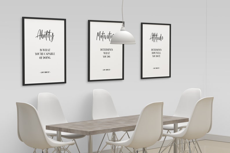 May include: Three black framed motivational posters with white text on a white wall. The posters are titled "Ability", "Motivation", and "Attitude". The text on the posters reads: "Ability is what you're capable of doing", "Motivation determines what you do", and "Attitude determines how well you do it".