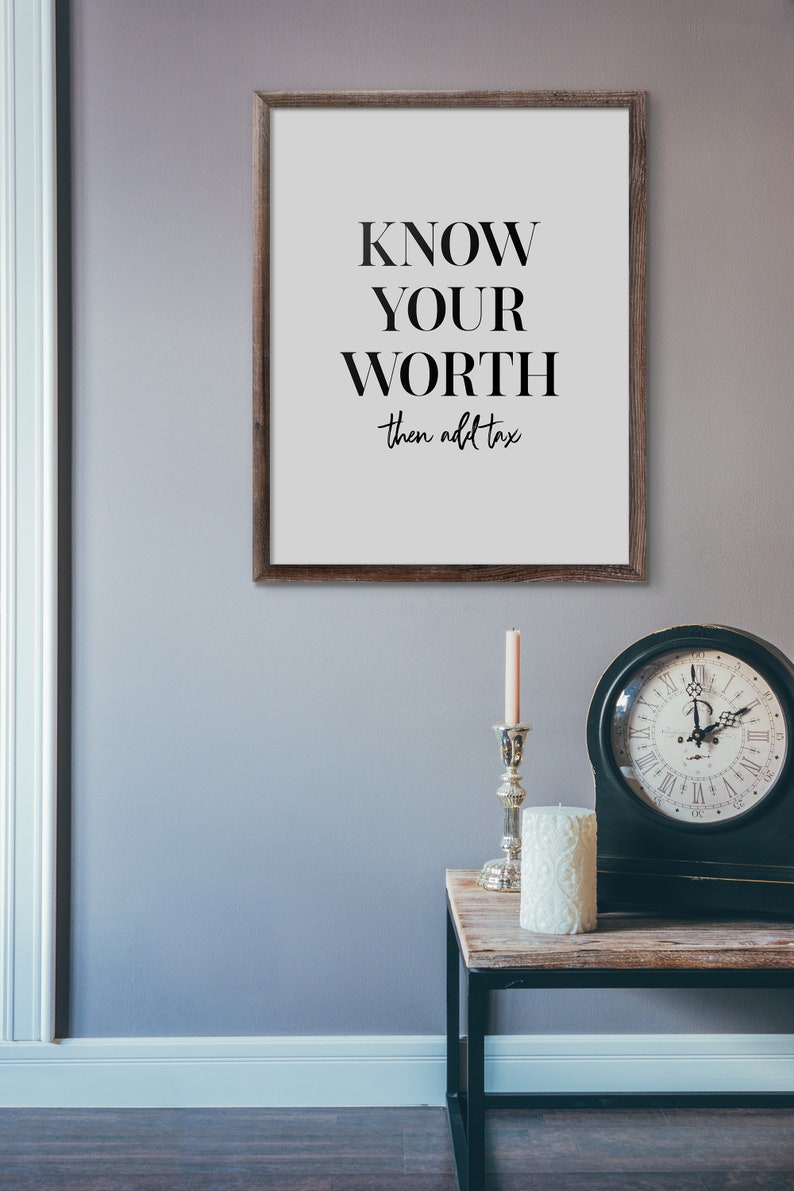 May include: A framed print with the text "KNOW YOUR WORTH then add tax" on a white background. The frame is brown wood. The print is hanging on a light grey wall.