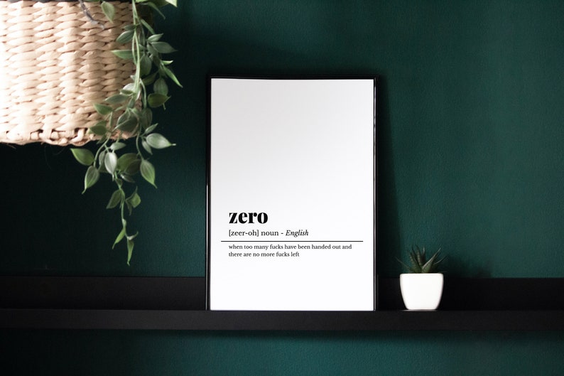 May include: A framed print with the definition of "zero" in black text on a white background. The definition includes the pronunciation and a humorous explanation. The frame is black, and the print is displayed against a dark green wall.