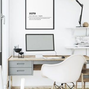 May include: A modern office setup featuring a desk with a computer, a white chair, and a framed print. The print has the word "zero" with a definition. A black desk lamp and decorative items complete the workspace.