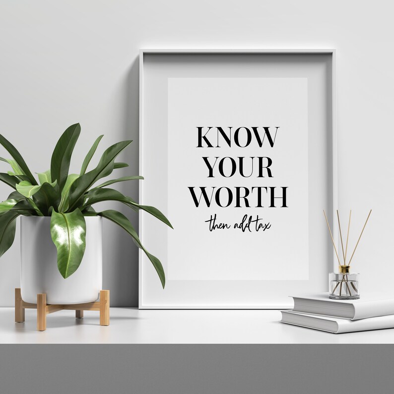 May include: A white framed print with the text "KNOW YOUR WORTH then add tax" in black lettering on a white background. The print is sitting on a white surface with a potted plant and a diffuser to the left and a stack of books to the right.