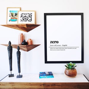 May include: A modern interior design scene featuring a white wall with floating wooden shelves. The shelves display framed art, vases, and sculptures. A large framed print reads "zero" with a definition. A wooden dresser holds a plant and books.