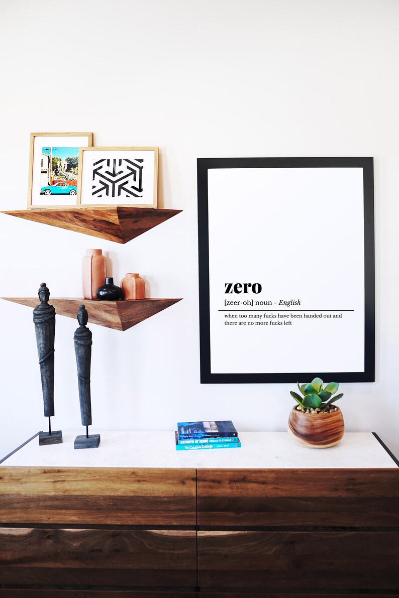 May include: A modern interior design scene featuring a white wall with floating wooden shelves. The shelves display framed art, vases, and sculptures. A large framed print reads "zero" with a definition. A wooden dresser holds a plant and books.