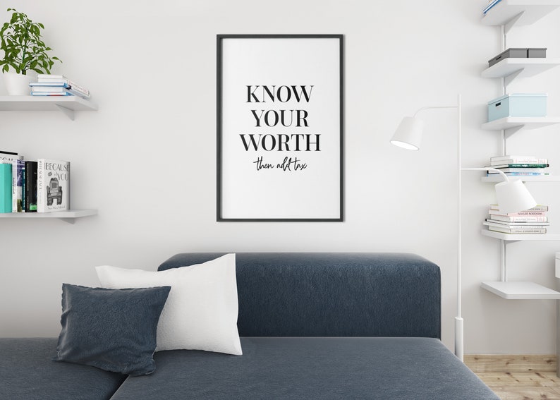 May include: A black and white framed print with the text "KNOW YOUR WORTH then add tax" hanging on a white wall in a living room setting.