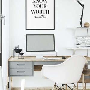 May include: A black framed poster with the text "KNOW YOUR WORTH then add tax" hanging on a white wall above a desk with a computer, a lamp, and a chair.
