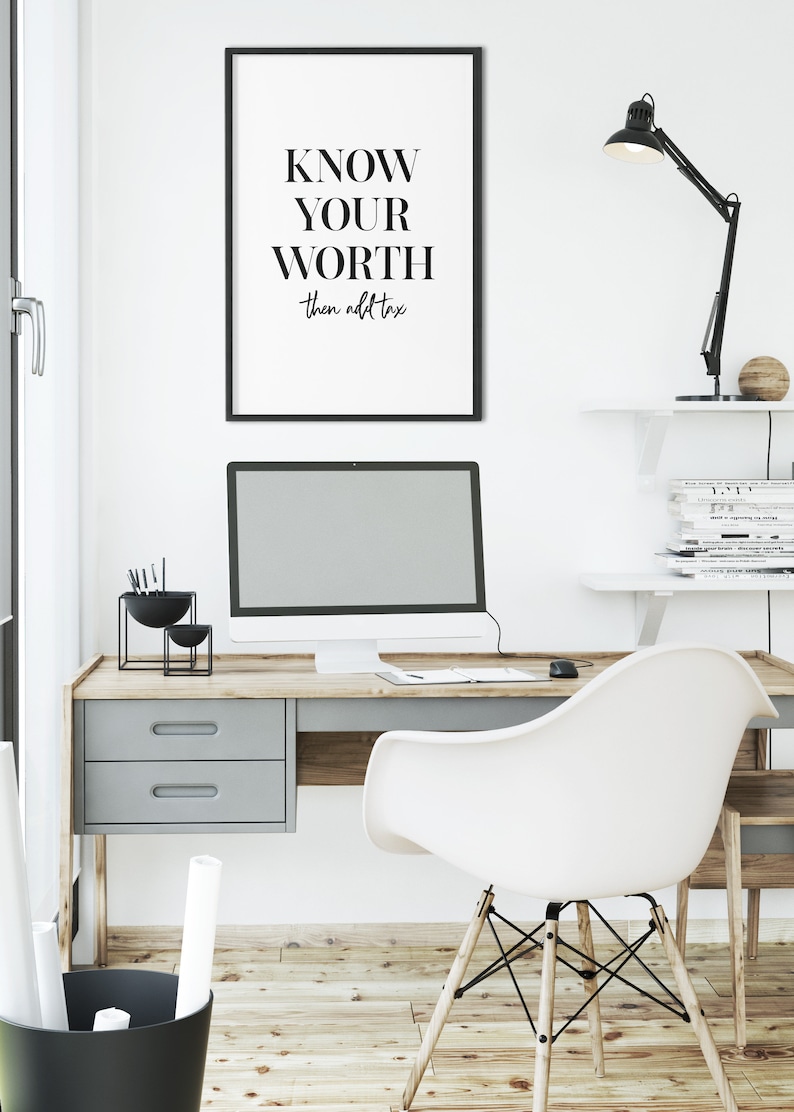 May include: A black framed poster with the text "KNOW YOUR WORTH then add tax" hanging on a white wall above a desk with a computer, a lamp, and a chair.