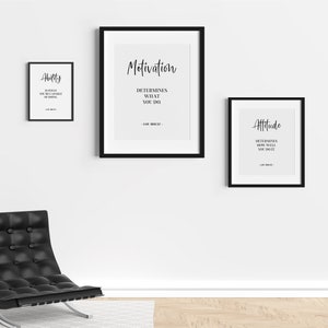 May include: Three black framed motivational posters with white text on a white wall. The posters read "Ability", "Motivation", and "Attitude". The posters are hanging above a black leather chair with a silver base.