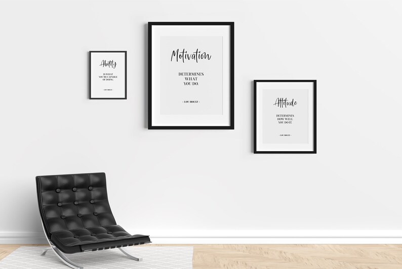 May include: Three black framed motivational posters with white text on a white wall. The posters read "Ability", "Motivation", and "Attitude". The posters are hanging above a black leather chair with a silver base.
