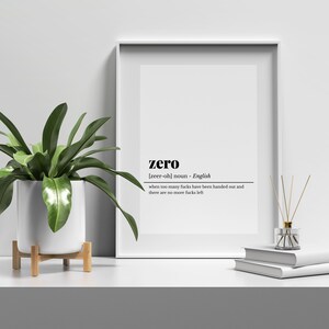 May include: A framed print with the word "zero" in a minimalist design. The definition below reads "when too many fucks have been handed out and there are no more fucks left." A potted plant and books are on the shelf.