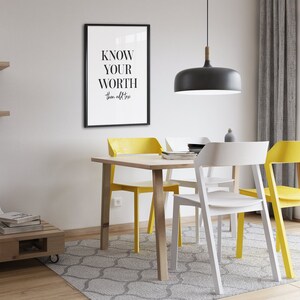 May include: A dining room with a wooden table and four chairs. Two chairs are yellow and two are white. The table has a framed print with the text "KNOW YOUR WORTH then add tax". A black pendant light hangs above the table.