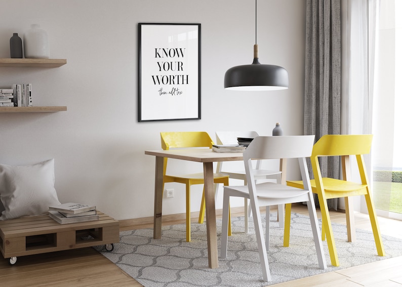 May include: A dining room with a wooden table and four chairs. Two chairs are yellow and two are white. The table has a framed print with the text "KNOW YOUR WORTH then add tax". A black pendant light hangs above the table.