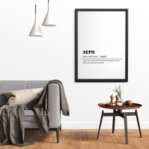May include: A framed black and white print with the definition of "zero". The print hangs above a gray sofa with a throw blanket and pillow. A small round table with a wooden top and black legs sits nearby.